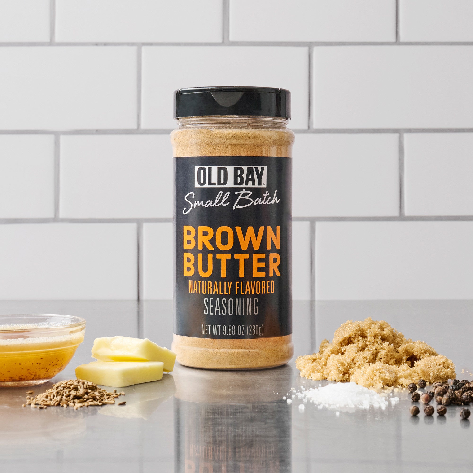 Old Bay Brown Butter seasoning jar on a kitchen counter with ingredients.