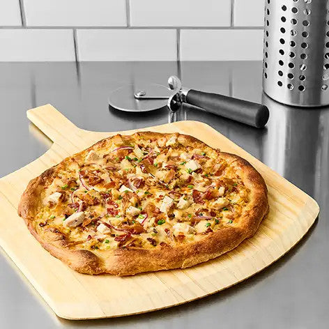 Pizza on a wooden board with a pizza cutter on a kitchen counter