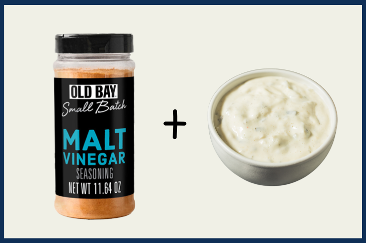 Old Bay malt vinegar seasoning jar next to a bowl of creamy sauce on a light background