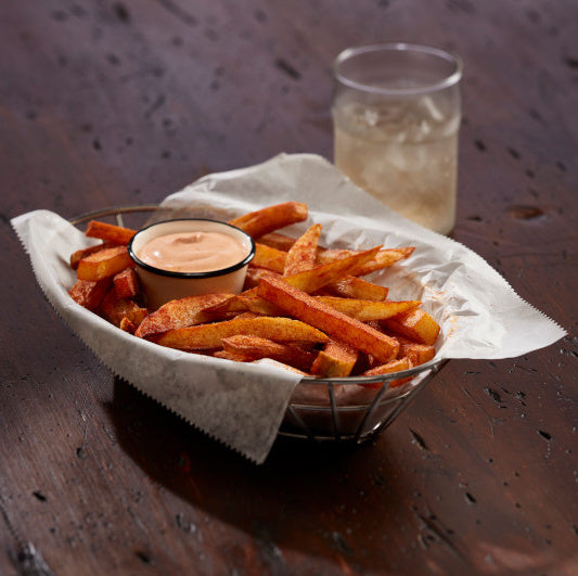 Bowl of fries with a dipping sauce and a glass of beer on a wooden table.