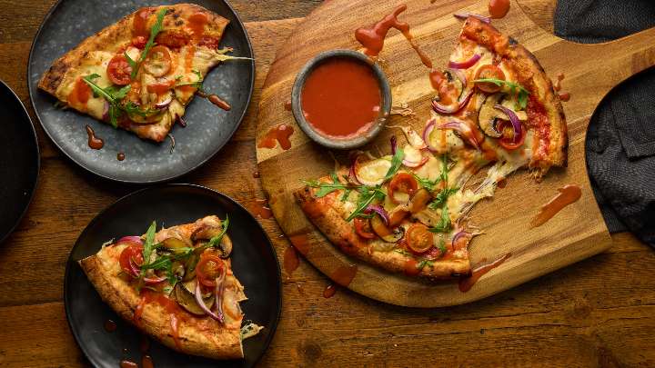 spicy veggie pizza on a pizza board cut into four slices and two of the slices are on black plates on a wooden table