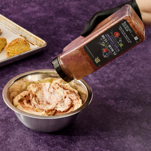 Bottle of black currant seasoning being poured into a bowl of food on a purple surface