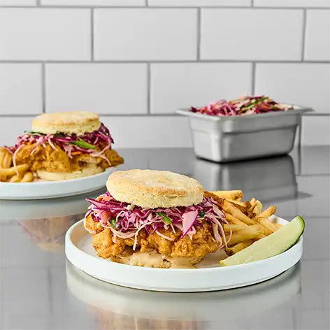 Burgers with fries and coleslaw on a reflective surface with a tiled wall background
