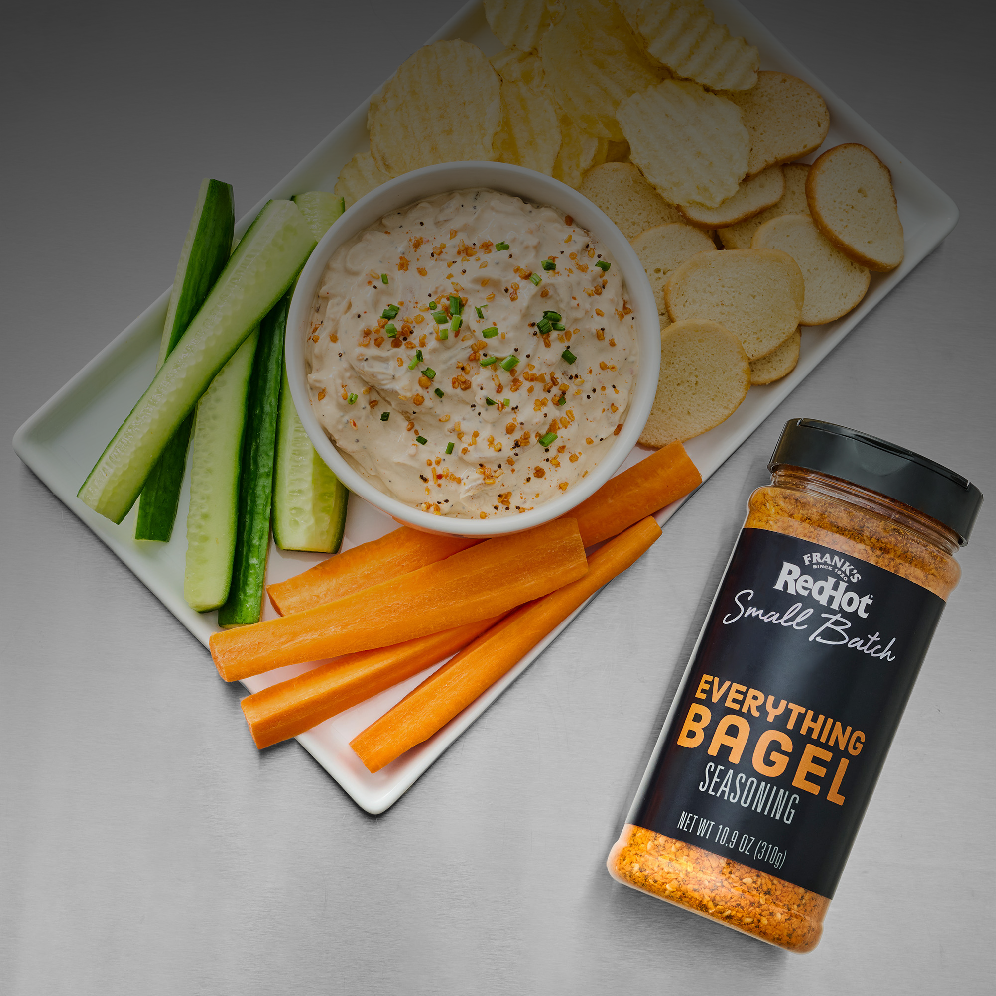 Platter of vegetables, dip, and bagel seasoning on a gray background