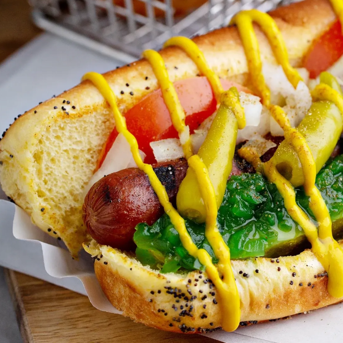 Hot dog with mustard, pickles, and other toppings on a bun.