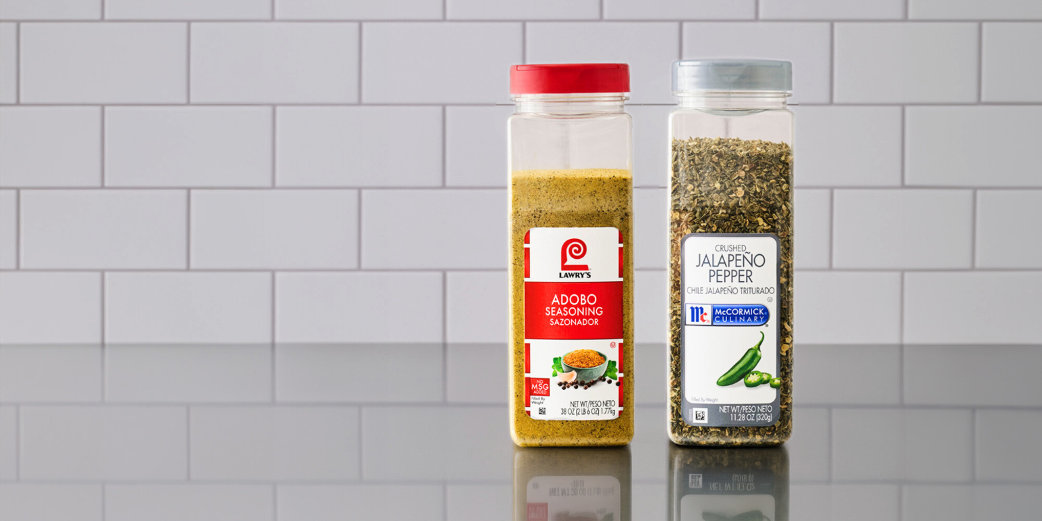 adobo seasoning and jalapeno pepper seasoning on a stainless steel counter with a white subway tile background