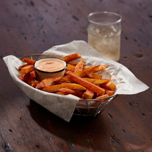 Bowl of fries with a dipping sauce and a glass of beer on a wooden table.